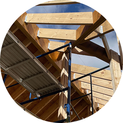 Wooden roof structure under construction, scaffolding visible, blue sky background.
