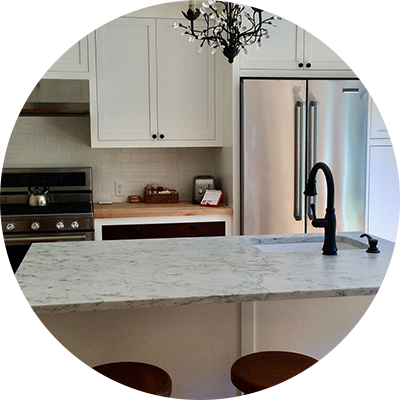 Kitchen with white cabinets, stainless steel refrigerator, marble countertop, and black faucet.