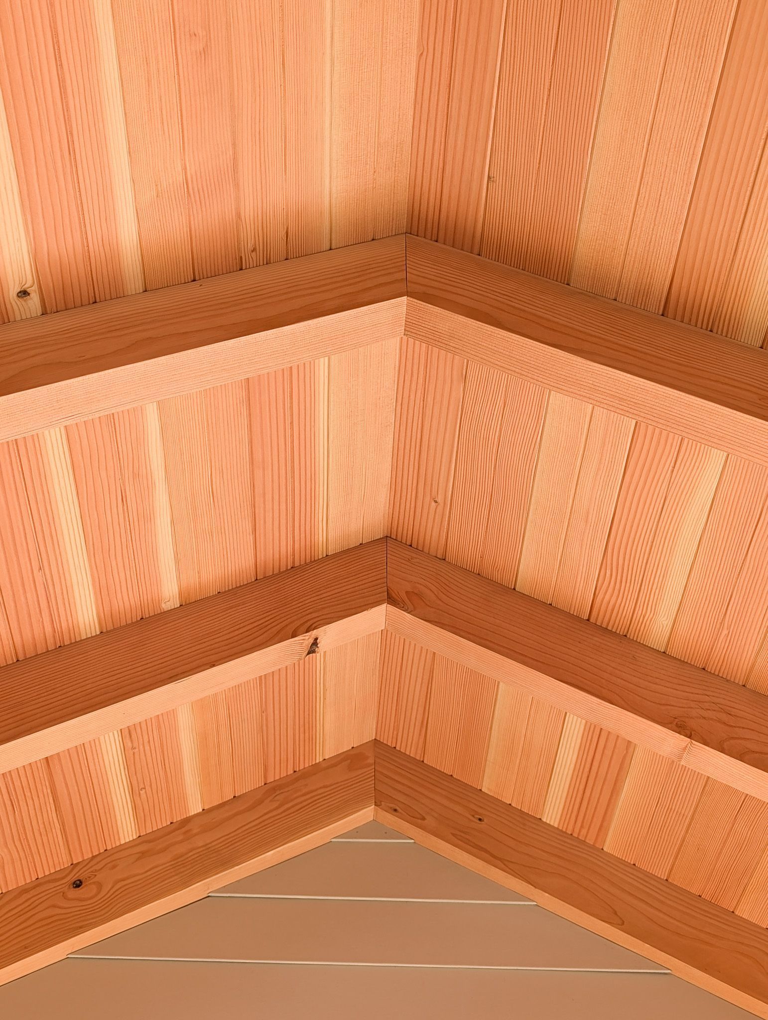 A corner view of wooden sauna benches made from vertical slats of light-colored cedar against matching wood walls.