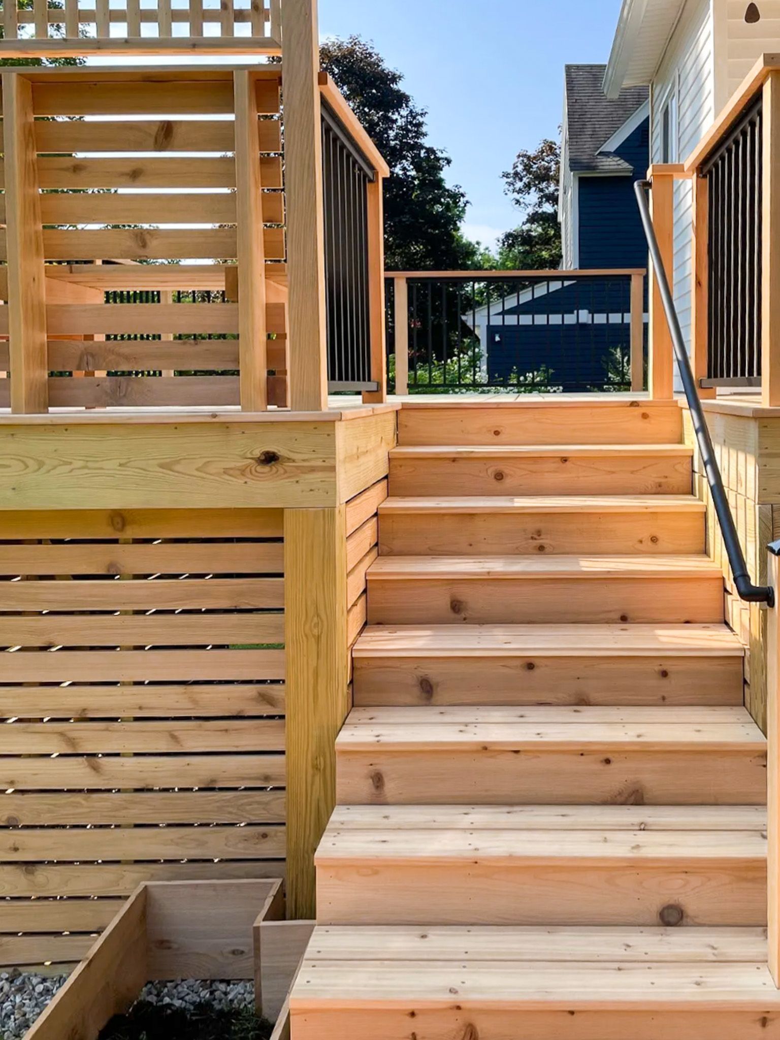 Wooden outdoor staircase leading to an elevated deck with slatted privacy screens and metal railings.