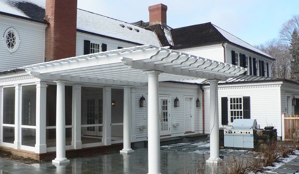 A large white house with a screened in porch and a pergola