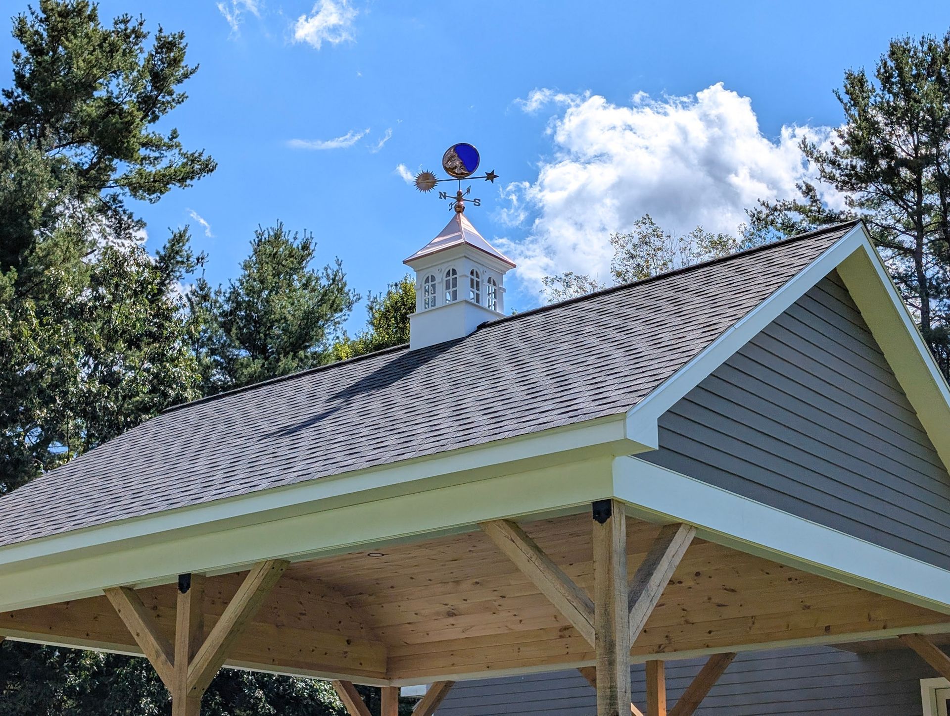 Pavilion with gray roof and blue weather vane against a bright sky.