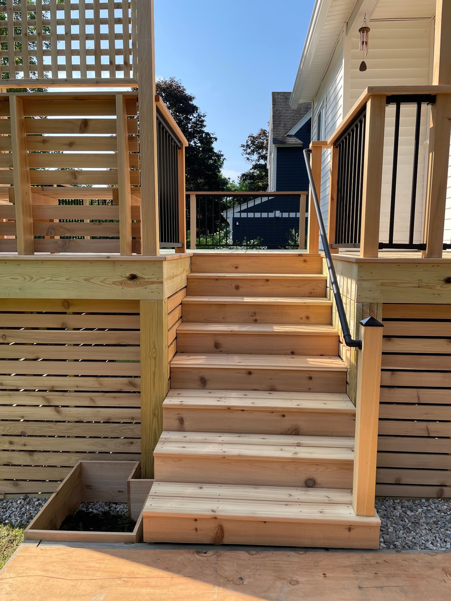 Wooden staircase leading up to a deck with horizontal siding and black metal railing.