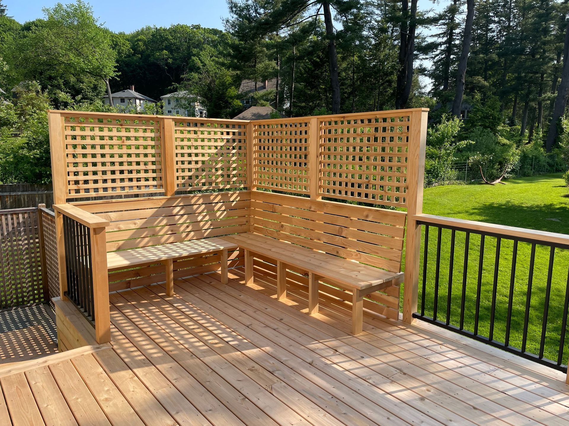 Wooden outdoor deck with built-in bench seating and trellis, in a sunny backyard setting.
