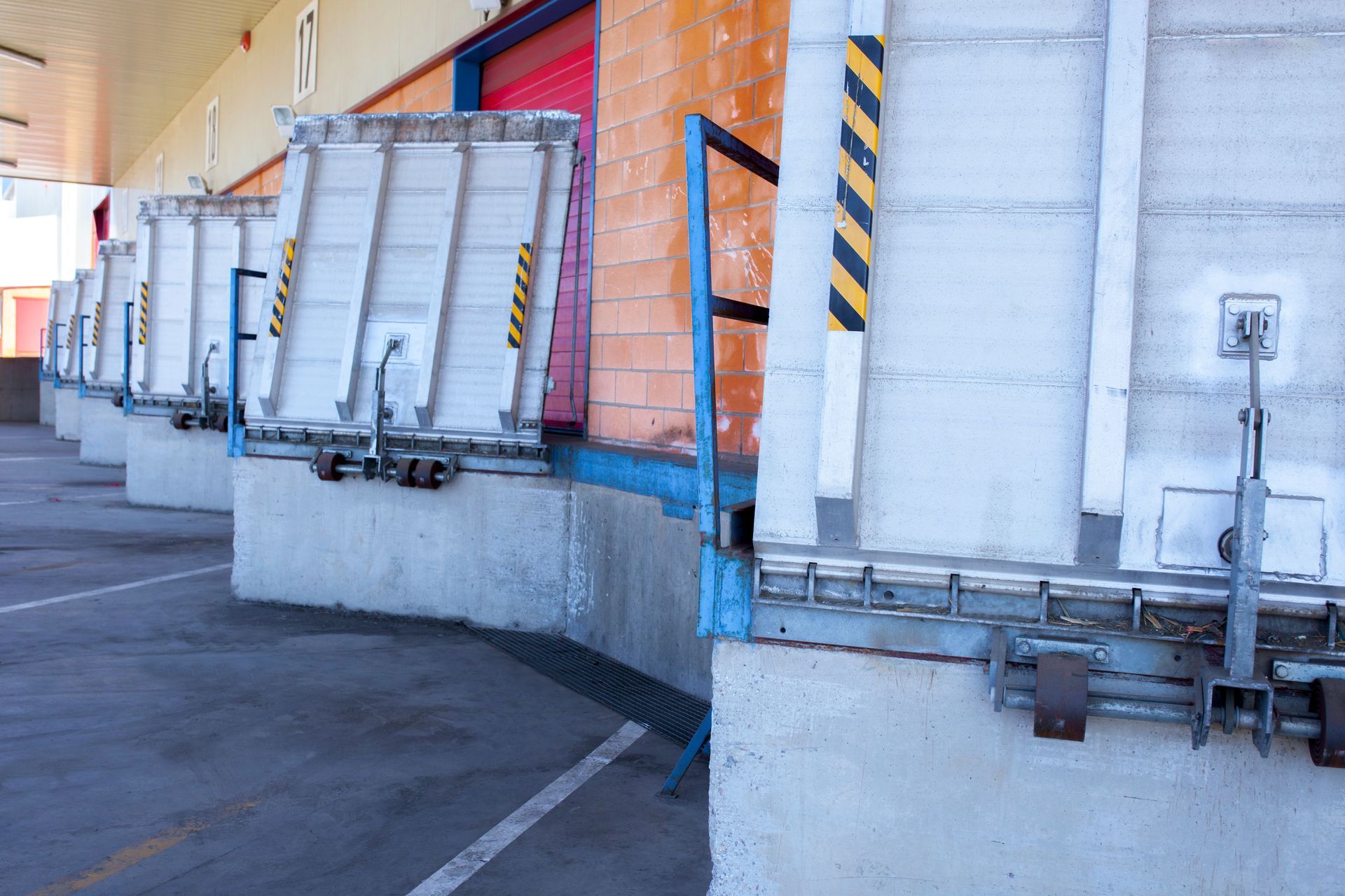 A row of loading docks at a warehouse with metal dock leveler plates standing in an upright position.