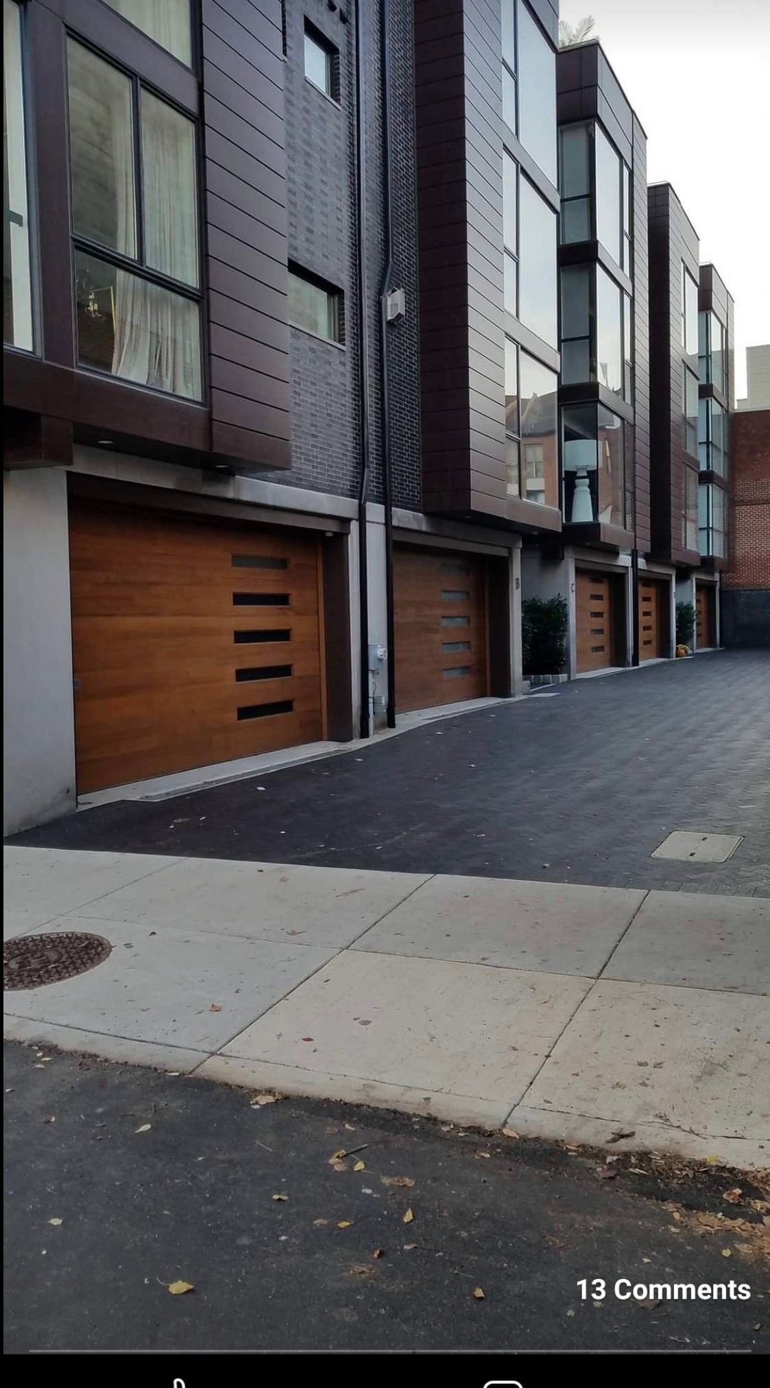 Modern townhouses with wooden garage doors line a paved alleyway in a city setting.