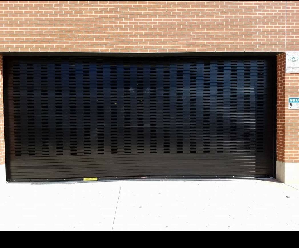 Black metal security roll-up door against a brick wall.