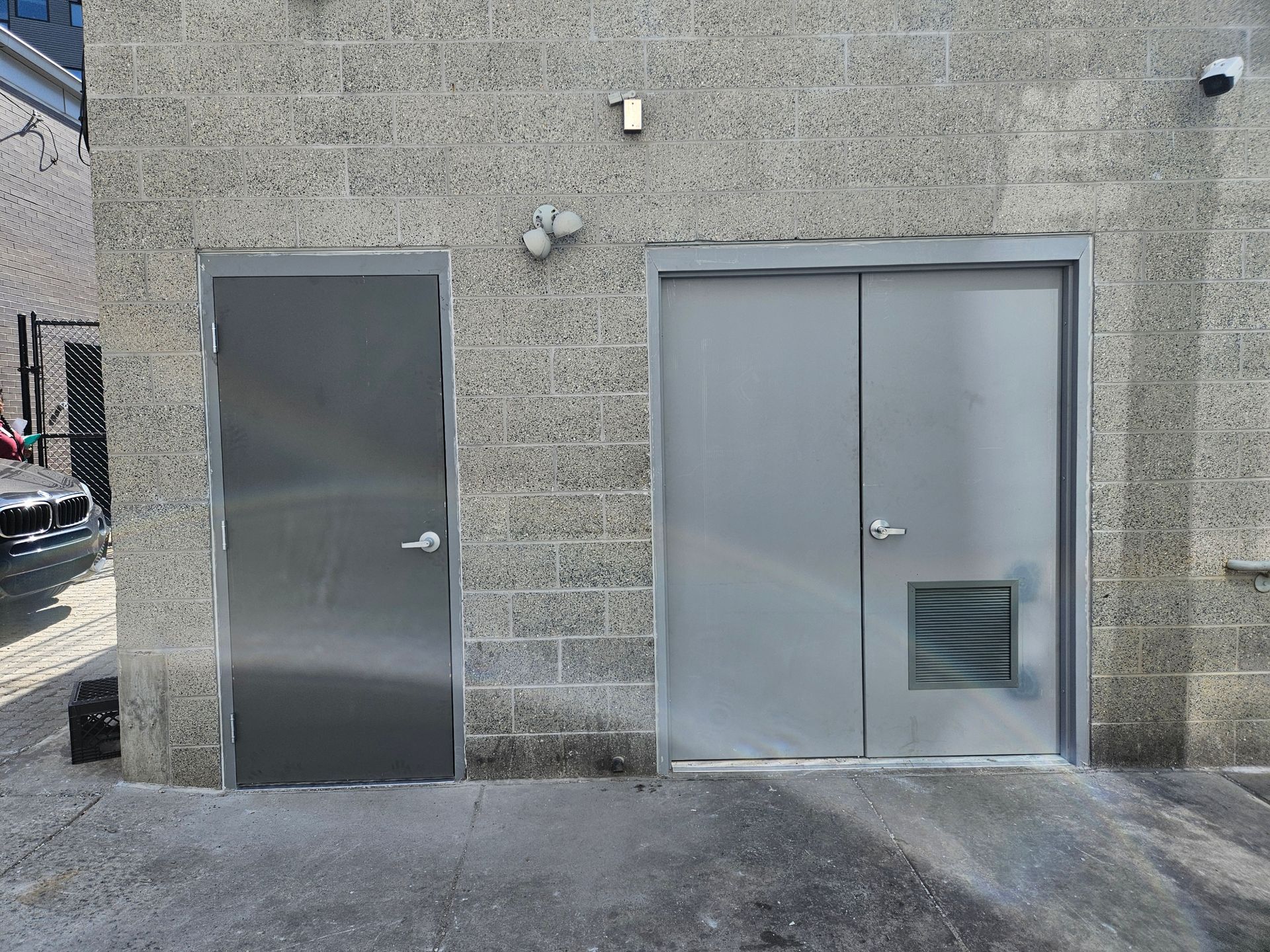 Two gray metal doors on a brick building with a camera and light.