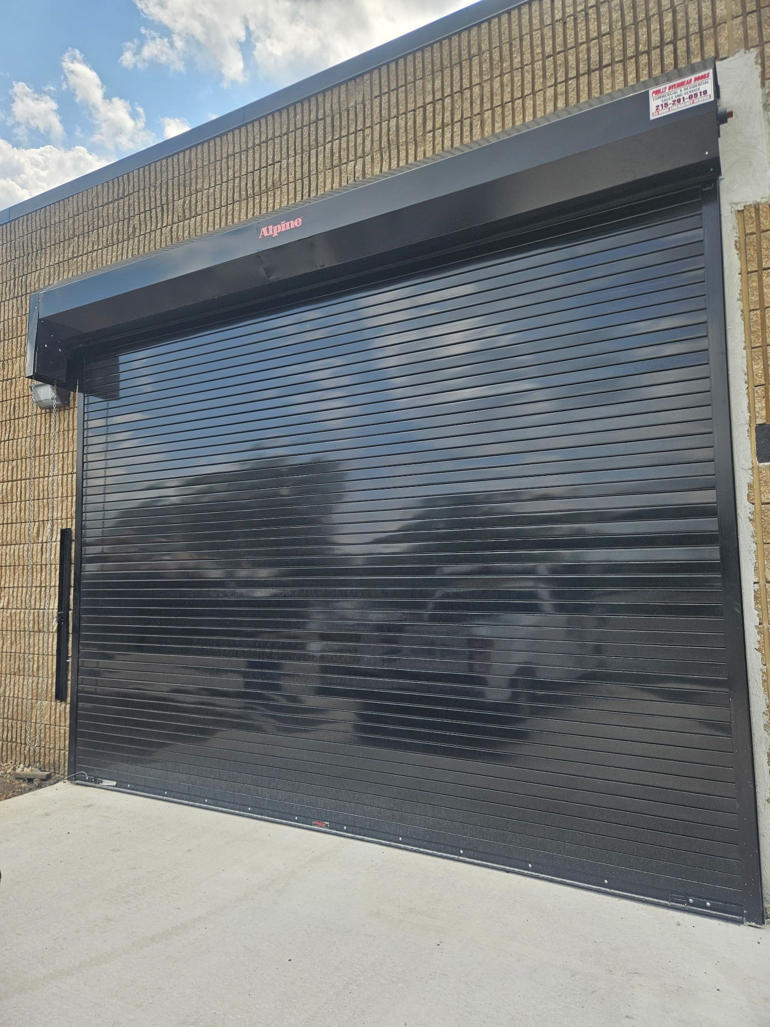 Black perforated rolling security door on a brick building with a concrete floor.