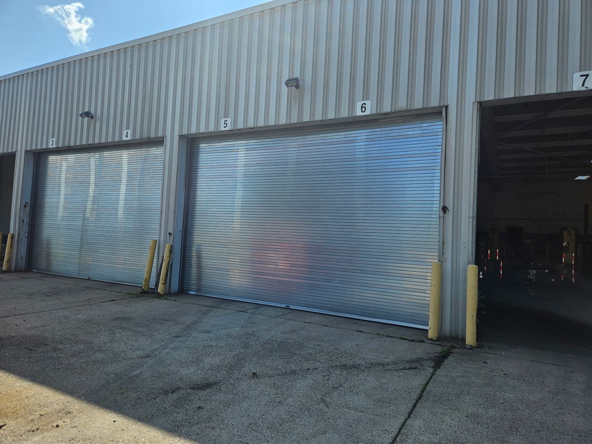 Metal roll-up doors on a warehouse exterior. Numbered loading bays. Sunny day.
