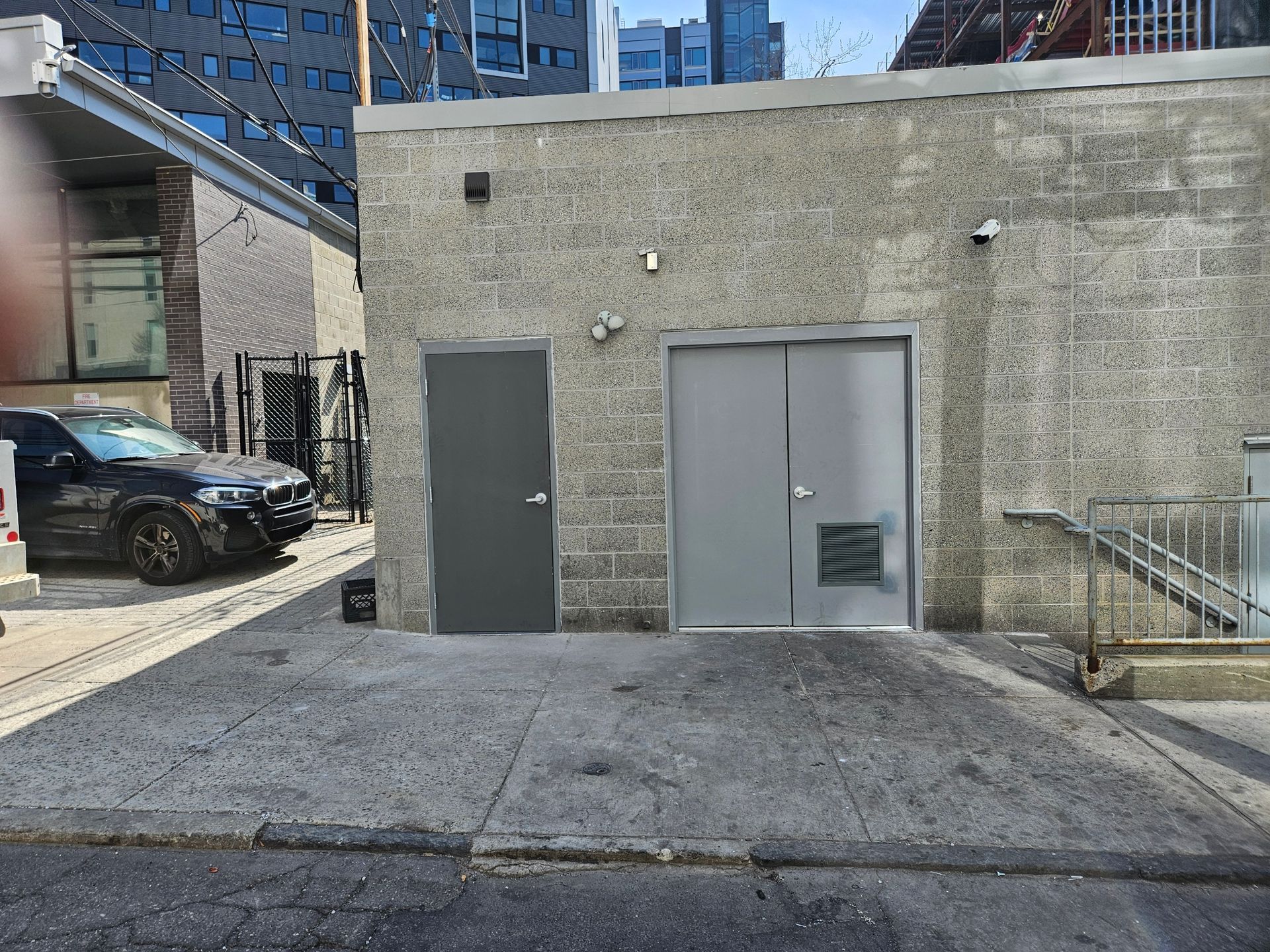 Exterior view of a gray concrete building with two doors. A black car is parked nearby.