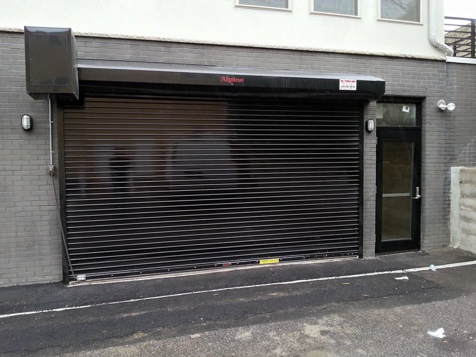 Black rolling shutter on a brick building with a black door.