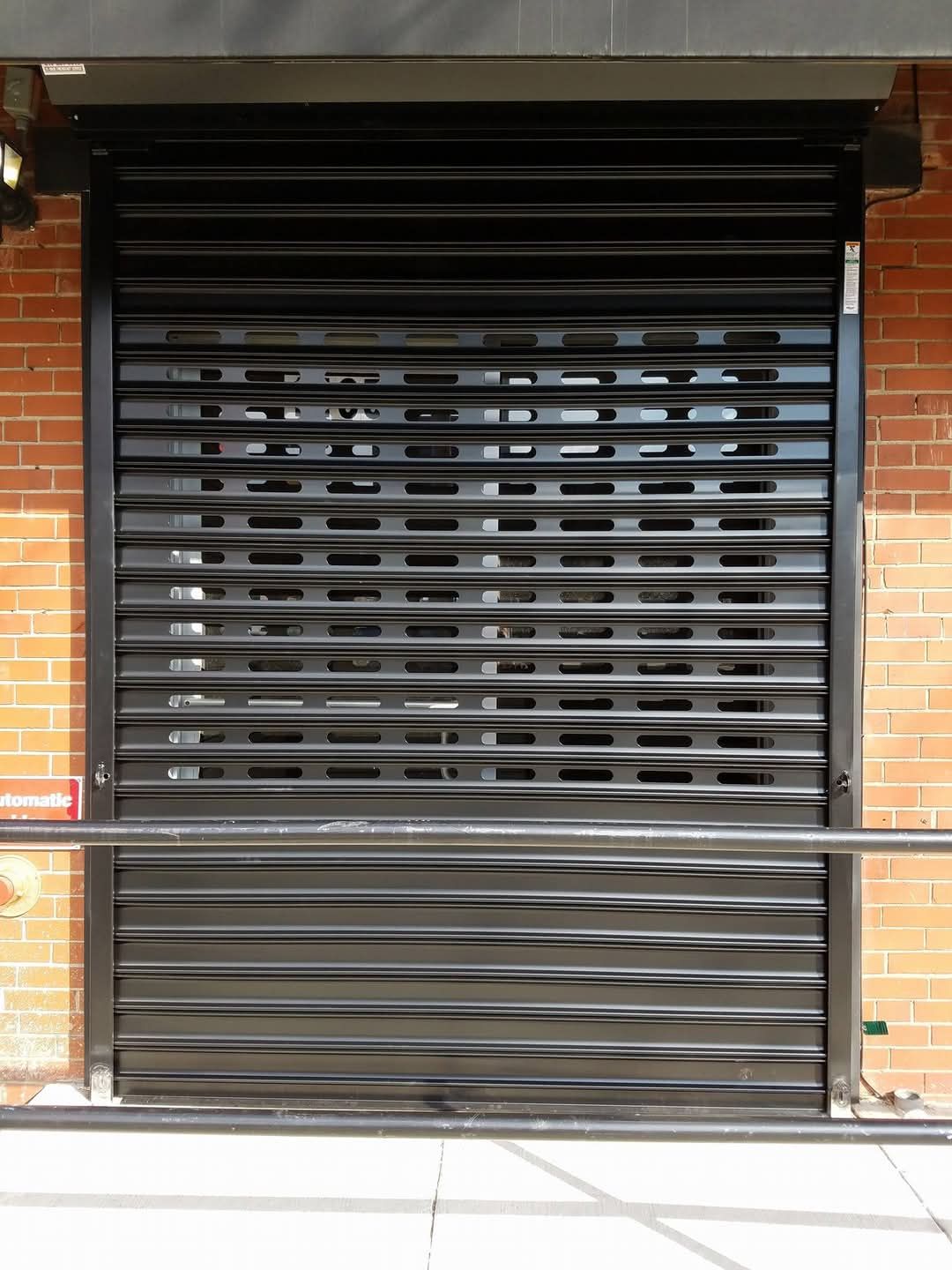 Black metal security shutter over a storefront window on a brick building.