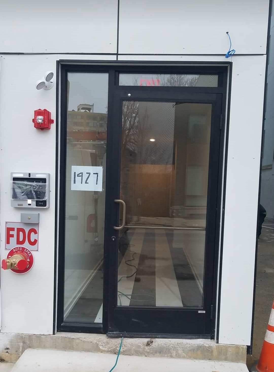 Exterior glass door of building 1927 with access panel, fire alarm, and FDC.