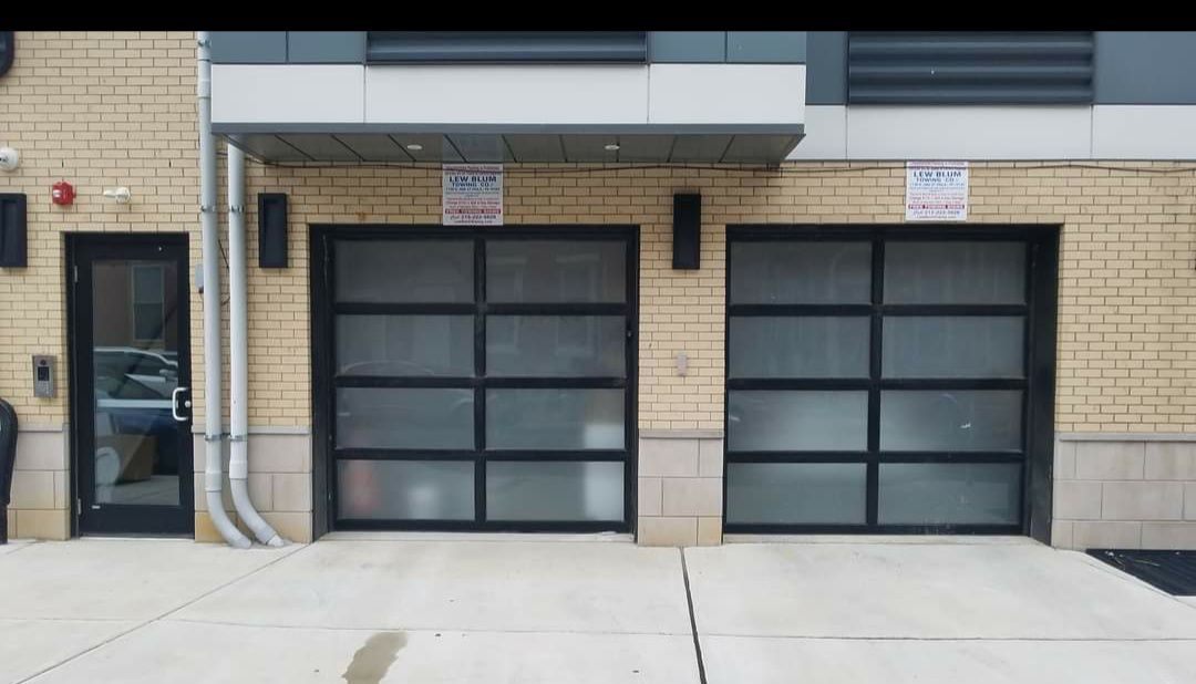 Exterior view of building with two garage doors and a glass door. Brick and concrete construction.