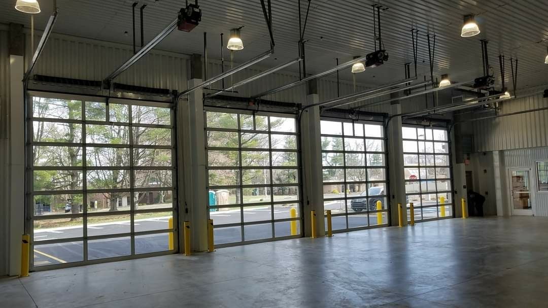 Interior of a building with three large glass garage doors open to the outside; concrete floor, gray ceiling.