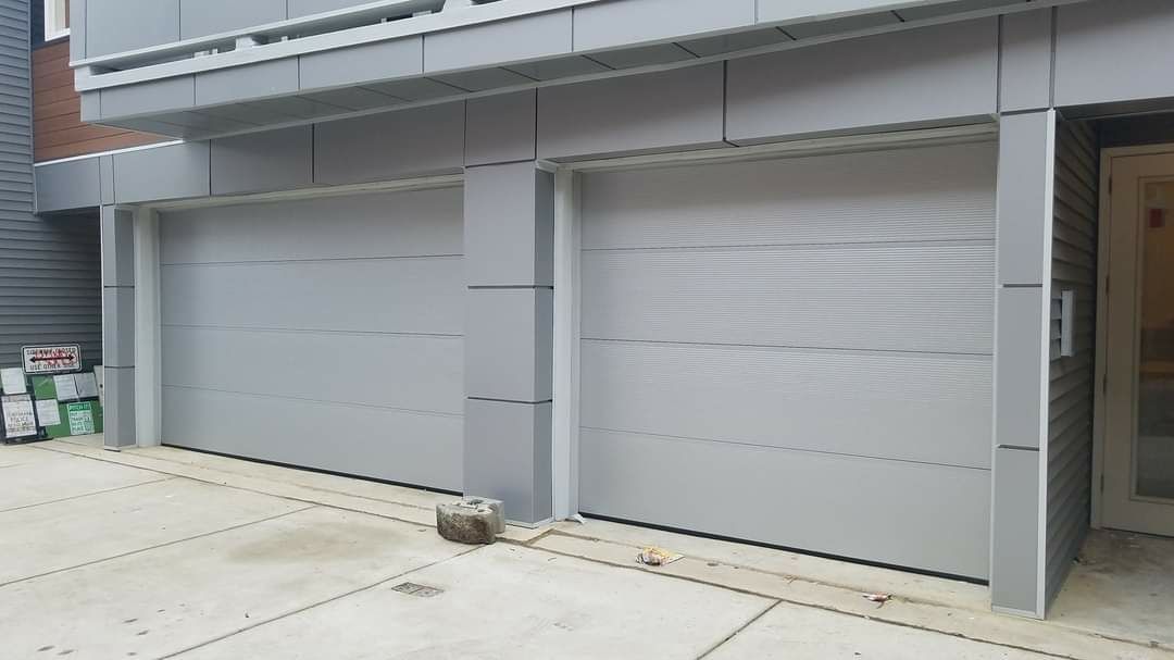 Two light gray garage doors with silver trim, concrete driveway.