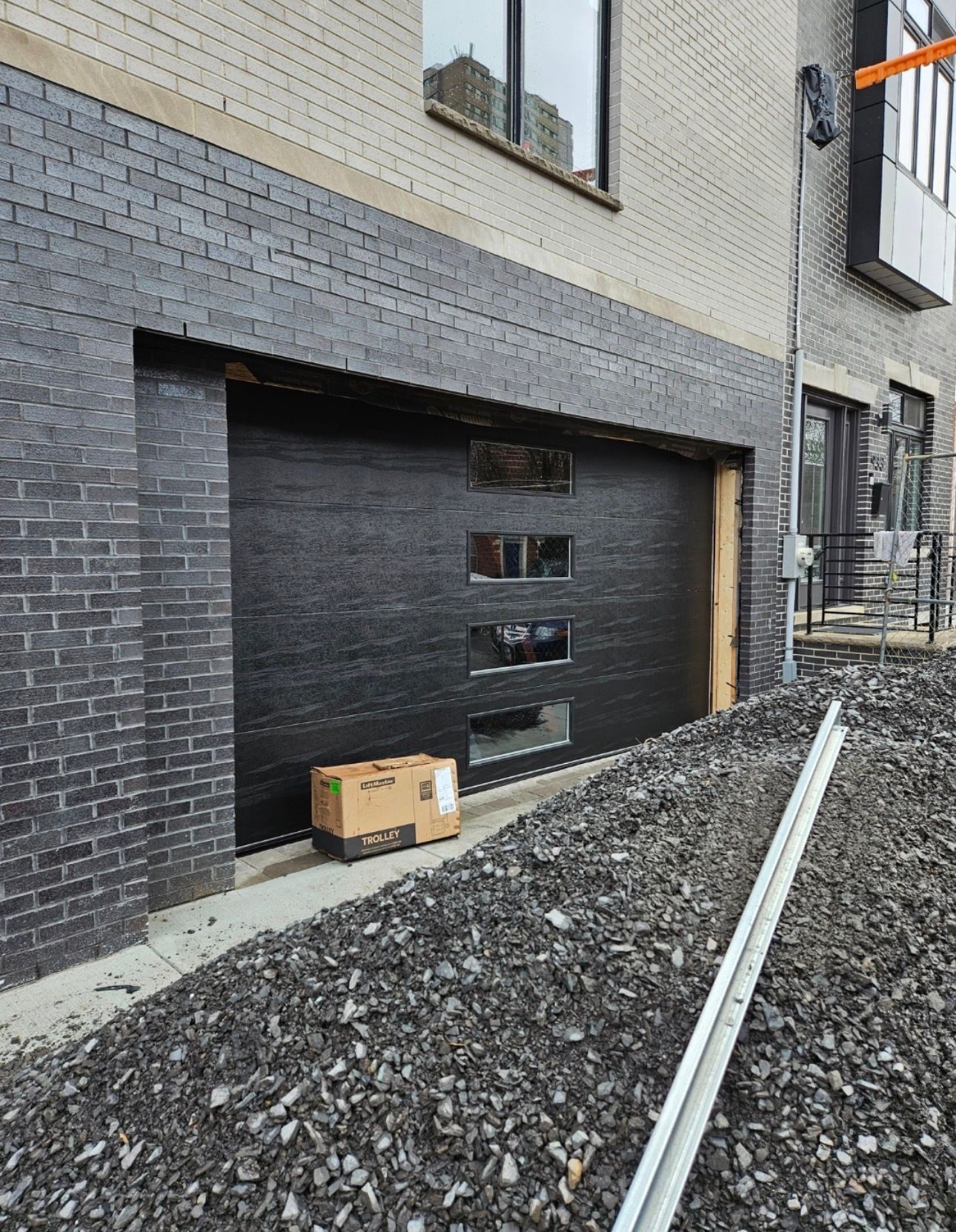 Garage door with black finish, brick facade, cardboard box on the ground.