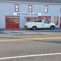 White truck parked in front of a glass shop with a red door and windows.