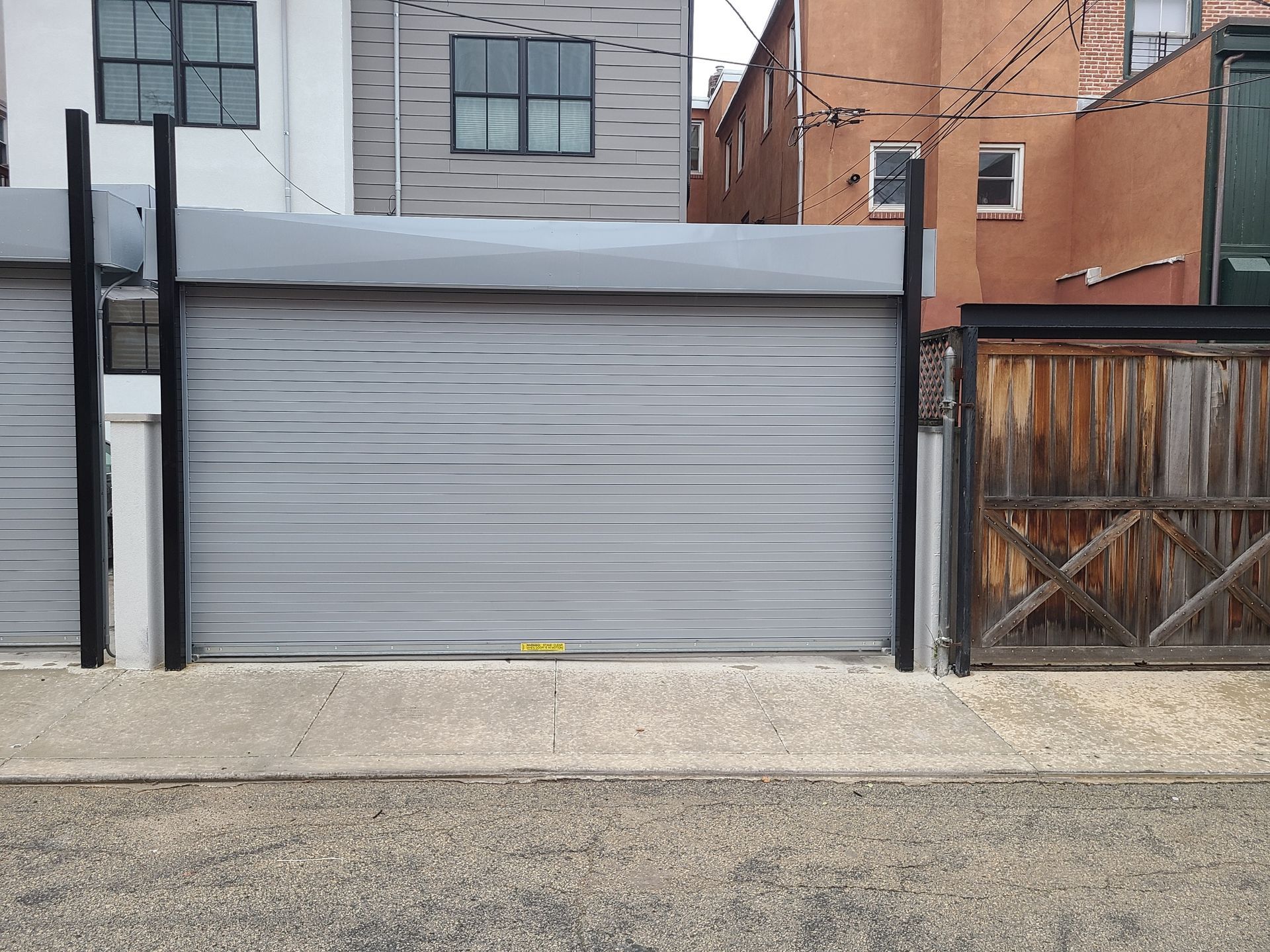 Gray garage door between black posts and a wooden gate.