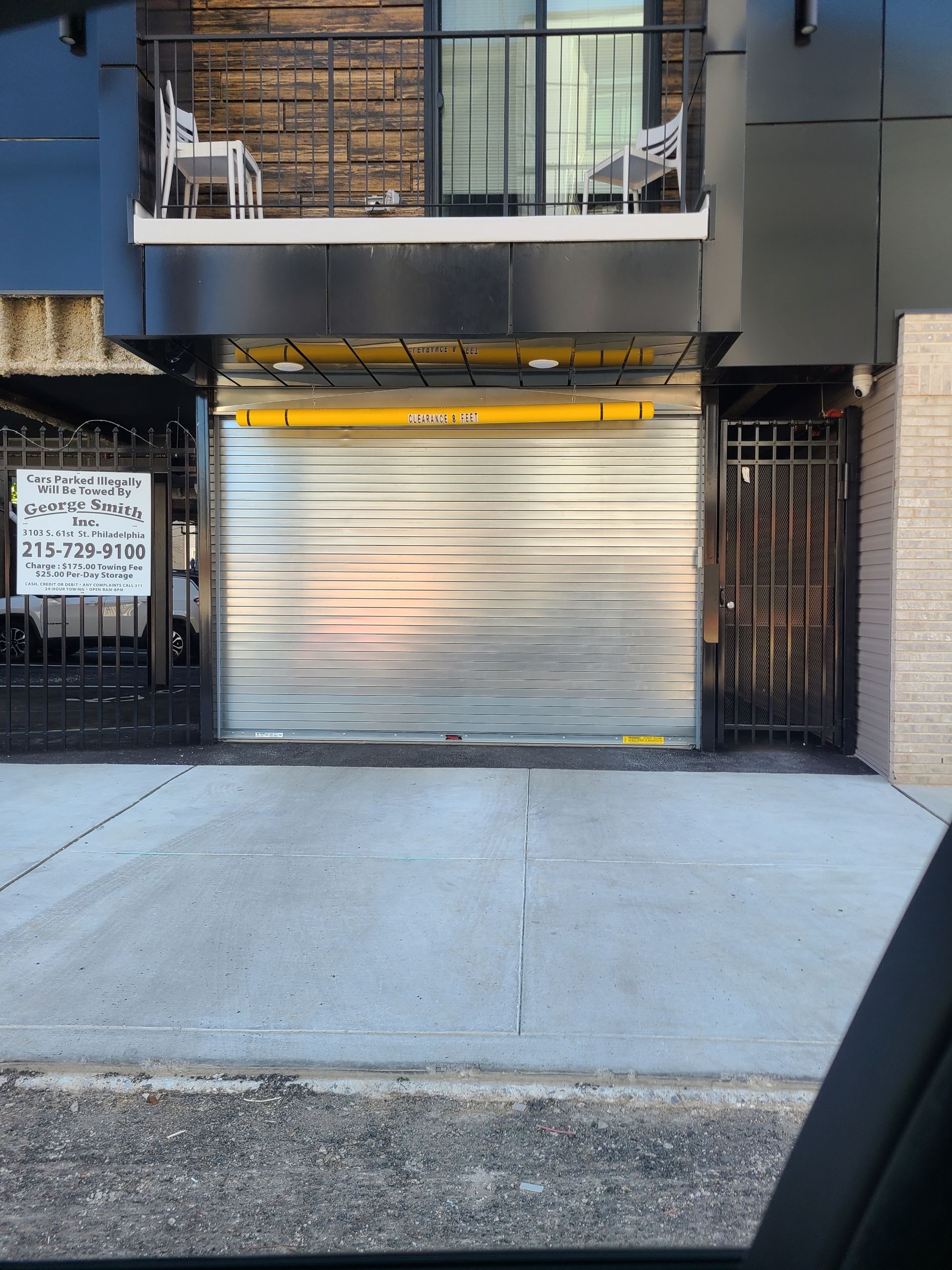 Exterior of building with closed silver garage door, black balcony above, and metal gate on either side.