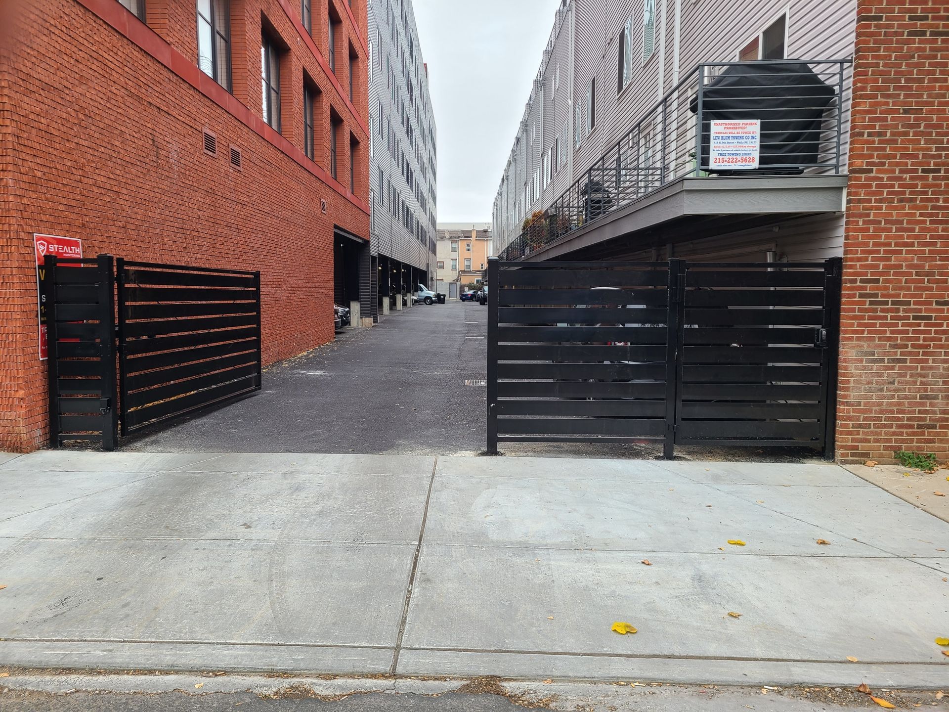 A narrow alleyway between brick buildings, with black fences and a concrete surface.