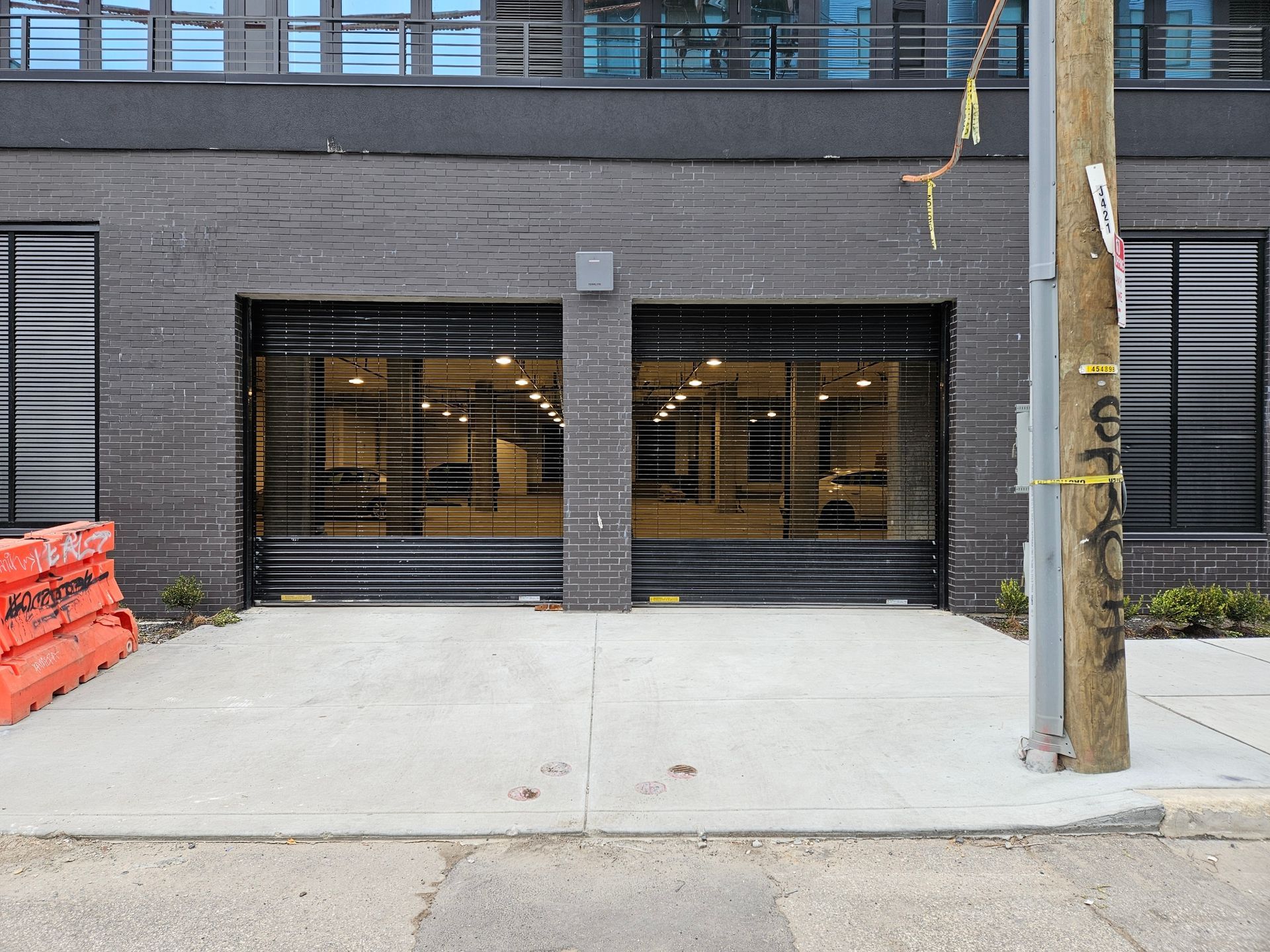 Two garage doors with a gray brick exterior. A sidewalk and utility pole are in the foreground.