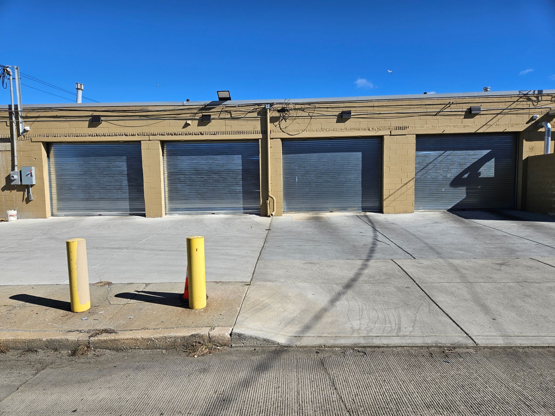 Row of three closed garage doors with concrete ramp, yellow bollards.
