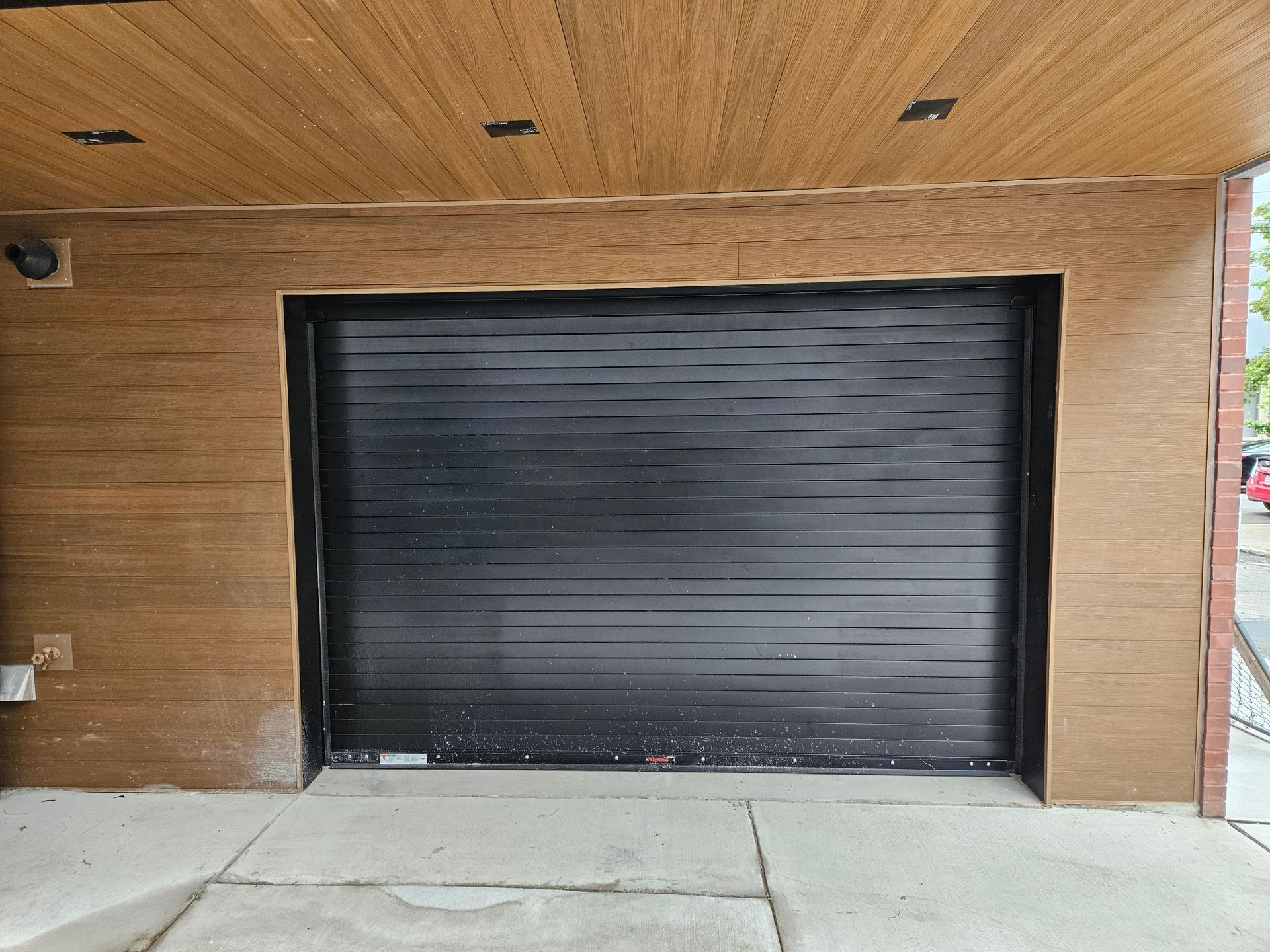 Black garage door with wood paneling on walls and ceiling. Concrete ground.