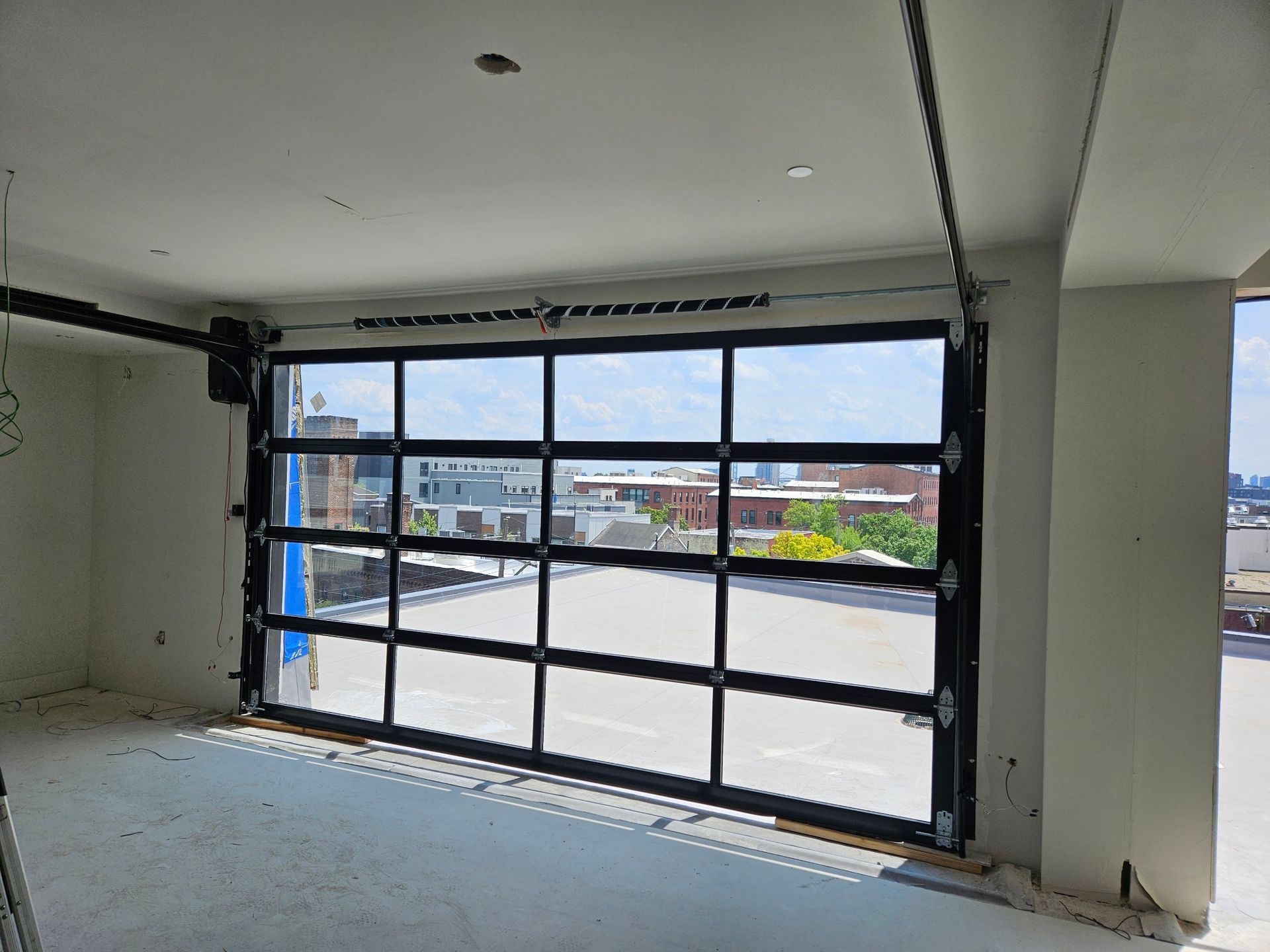 Glass garage door in a room overlooking an urban cityscape; black frame, white walls.