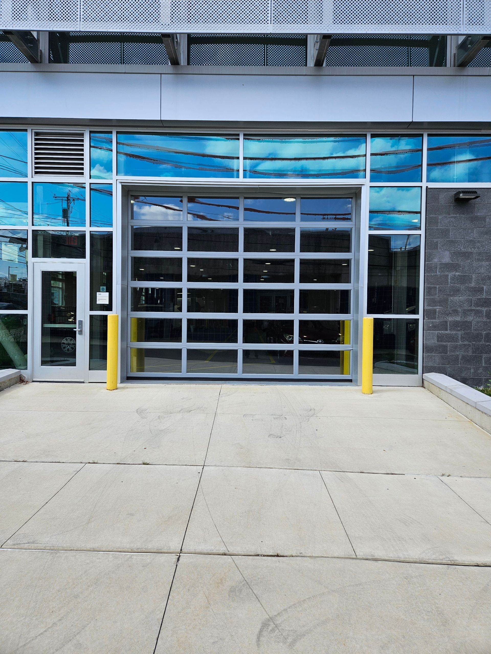 A modern building entrance with a large glass garage-style door and glass windows reflecting the sky.