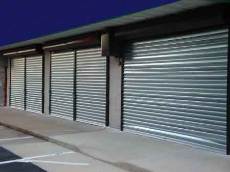 Row of closed, silver metal roller shutter doors on a building, under a dark sky.