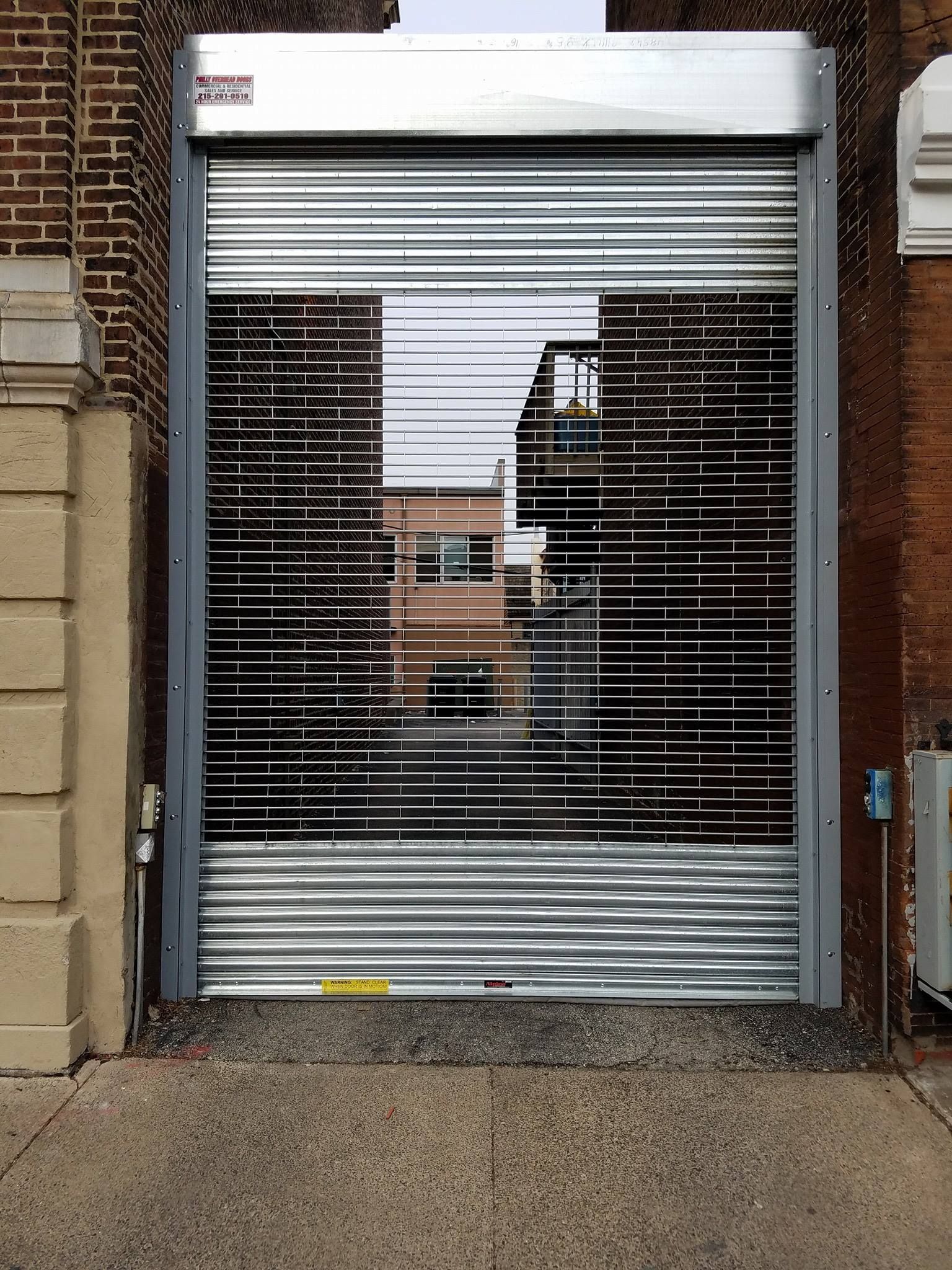 A metal rolling gate pulled partially down, revealing an alleyway between two brick buildings.