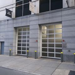 Two white-framed, grid-paneled garage doors in a gray stone building. Yellow bollards and a ramp are in front.