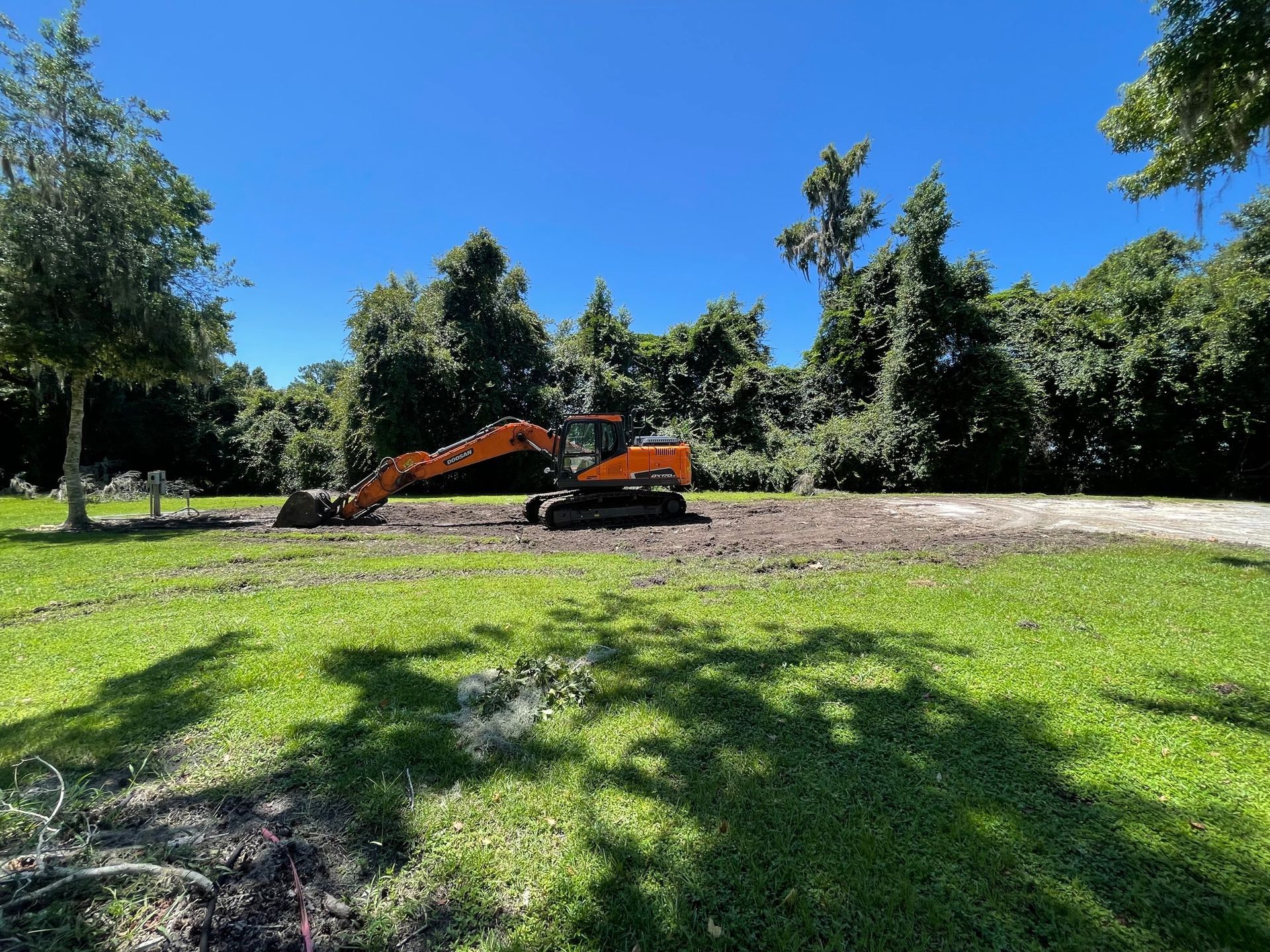 A large orange excavator is sitting in the middle of a lush green field.