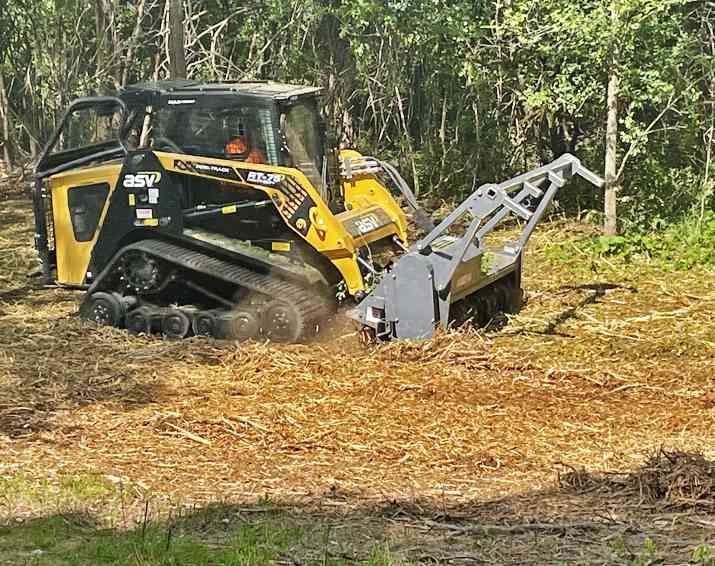 a yellow and black tractor is cutting down trees in the woods