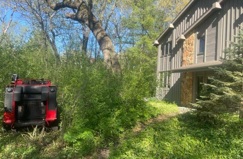 A house is surrounded by trees and bushes and a tractor is in the foreground.