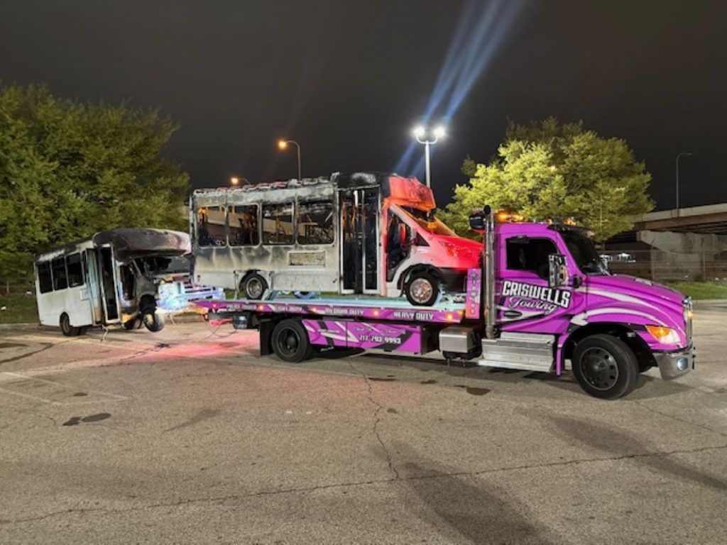 Tow truck loading a damaged bus at night in a lit parking lot