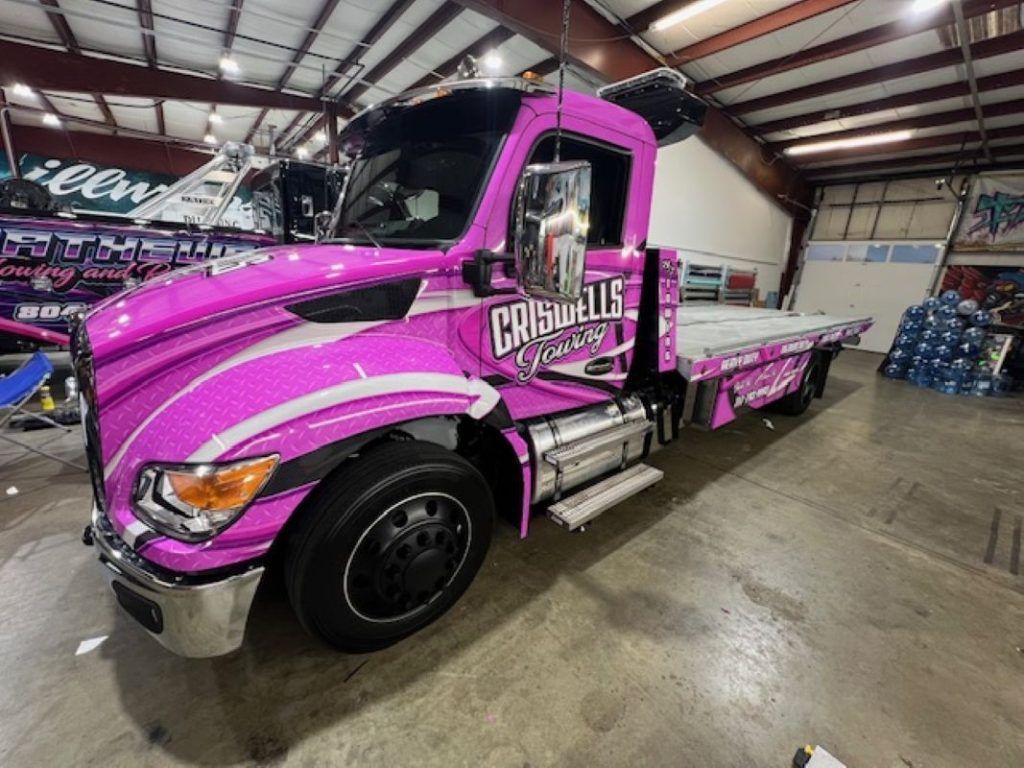 Pink and black custom tow truck in a warehouse garage, side view
