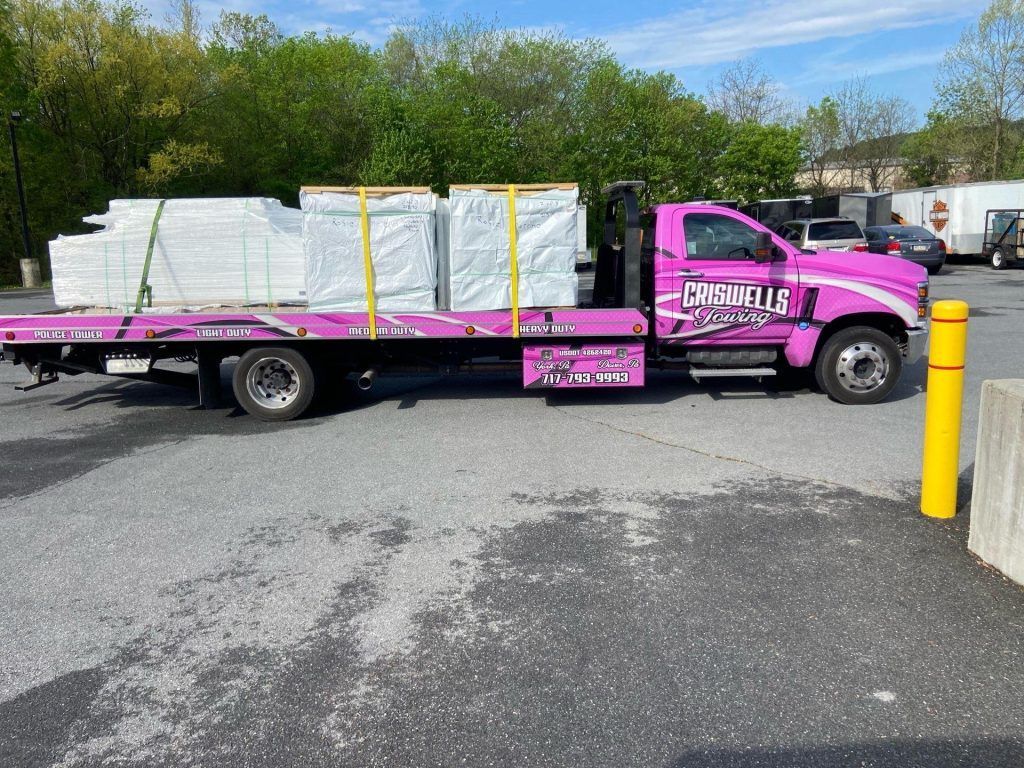 Pink flatbed truck loaded with wrapped pallets in a parking lot