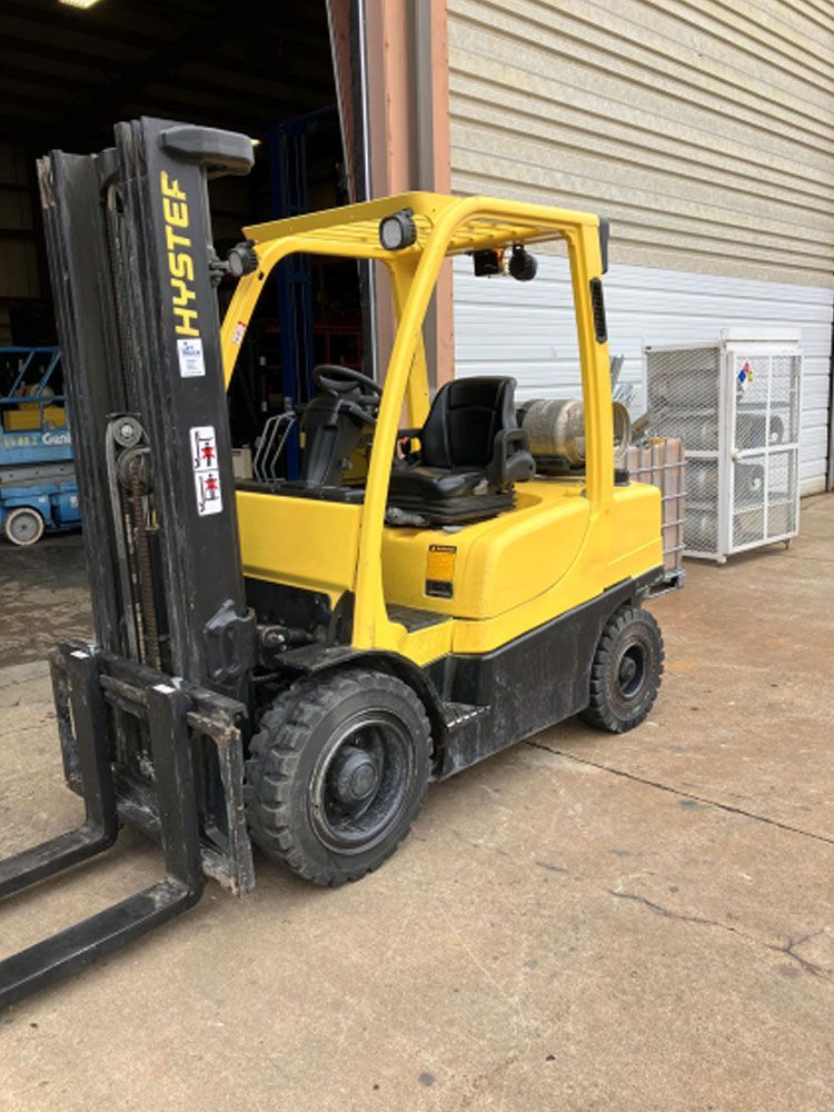 A yellow forklift is parked in front of a building.