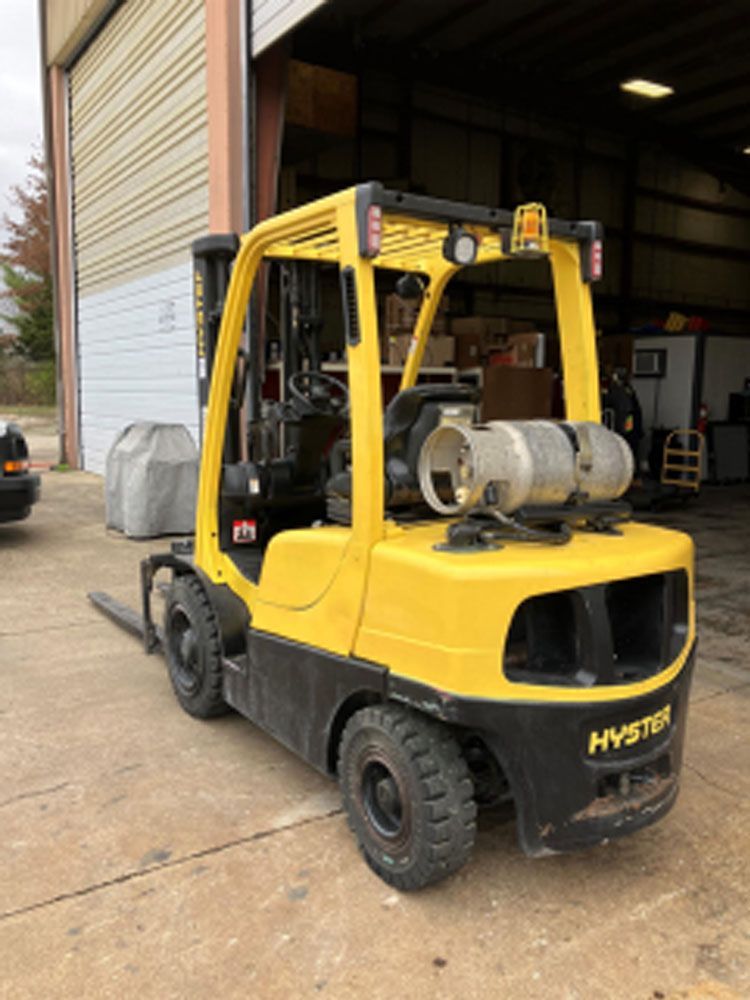 A yellow hyster forklift is parked in front of a building.