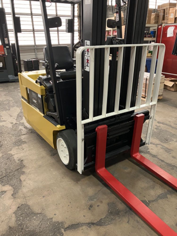 A yellow forklift with red forks is parked in a warehouse.