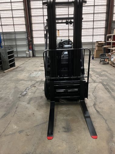 A forklift is parked in a warehouse with red forks.