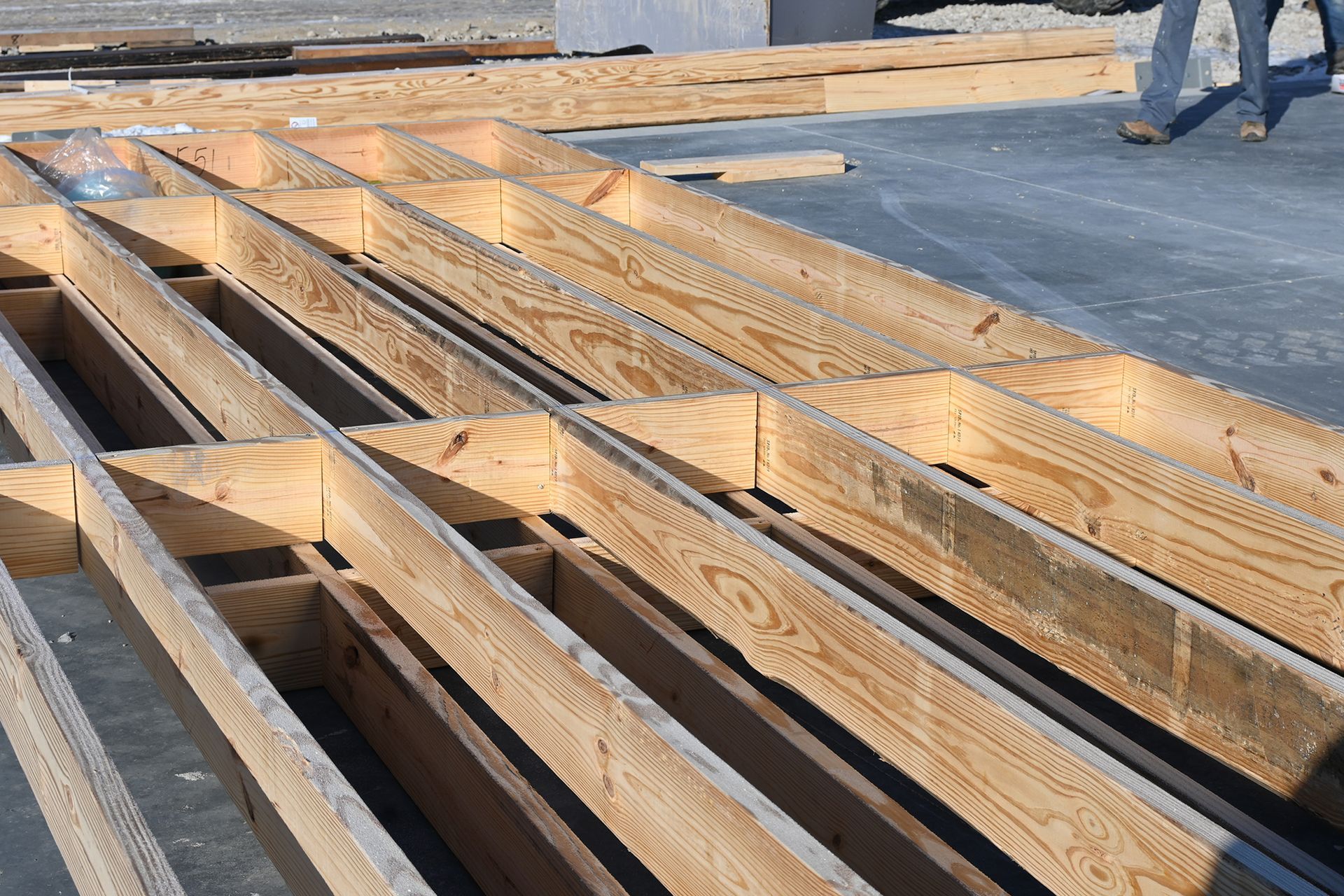 A person is standing next to a stack of wooden beams