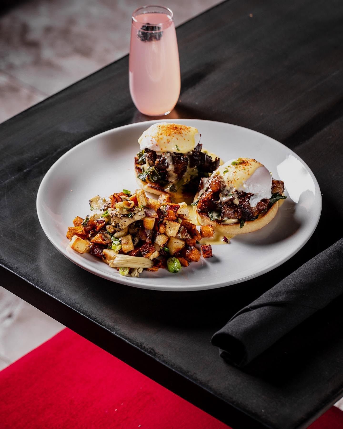 Plated gourmet dish with diced vegetables and poached eggs on a dark table, beside a pink drink.