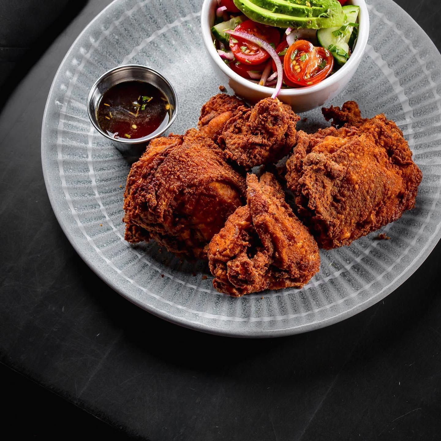 Fried chicken on a gray plate with dipping sauce and a small salad bowl on a dark table