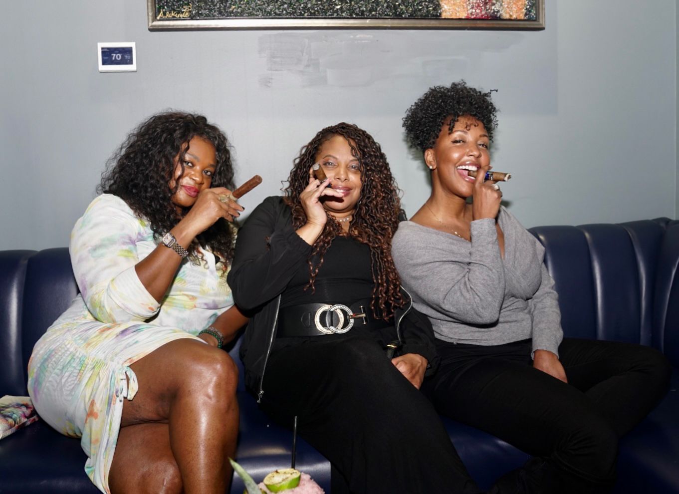 Three friends sitting on a couch, laughing and taking a selfie together.