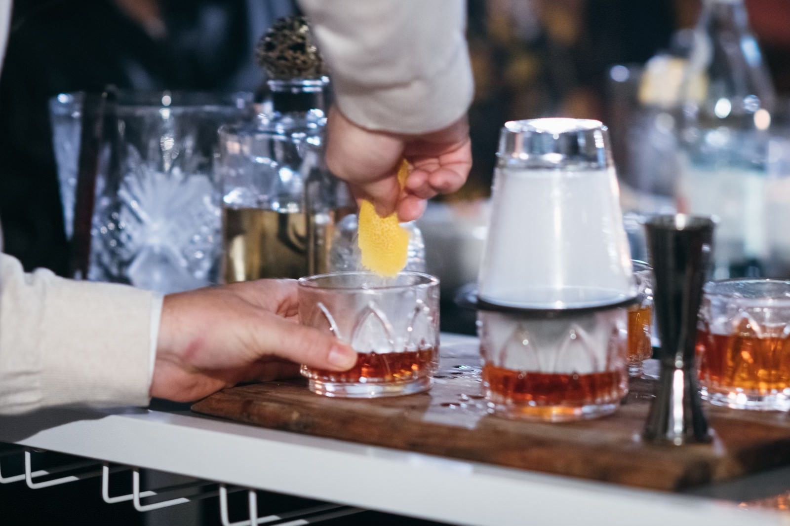 Bartender squeezing orange peel into a whiskey glass behind a bar counter