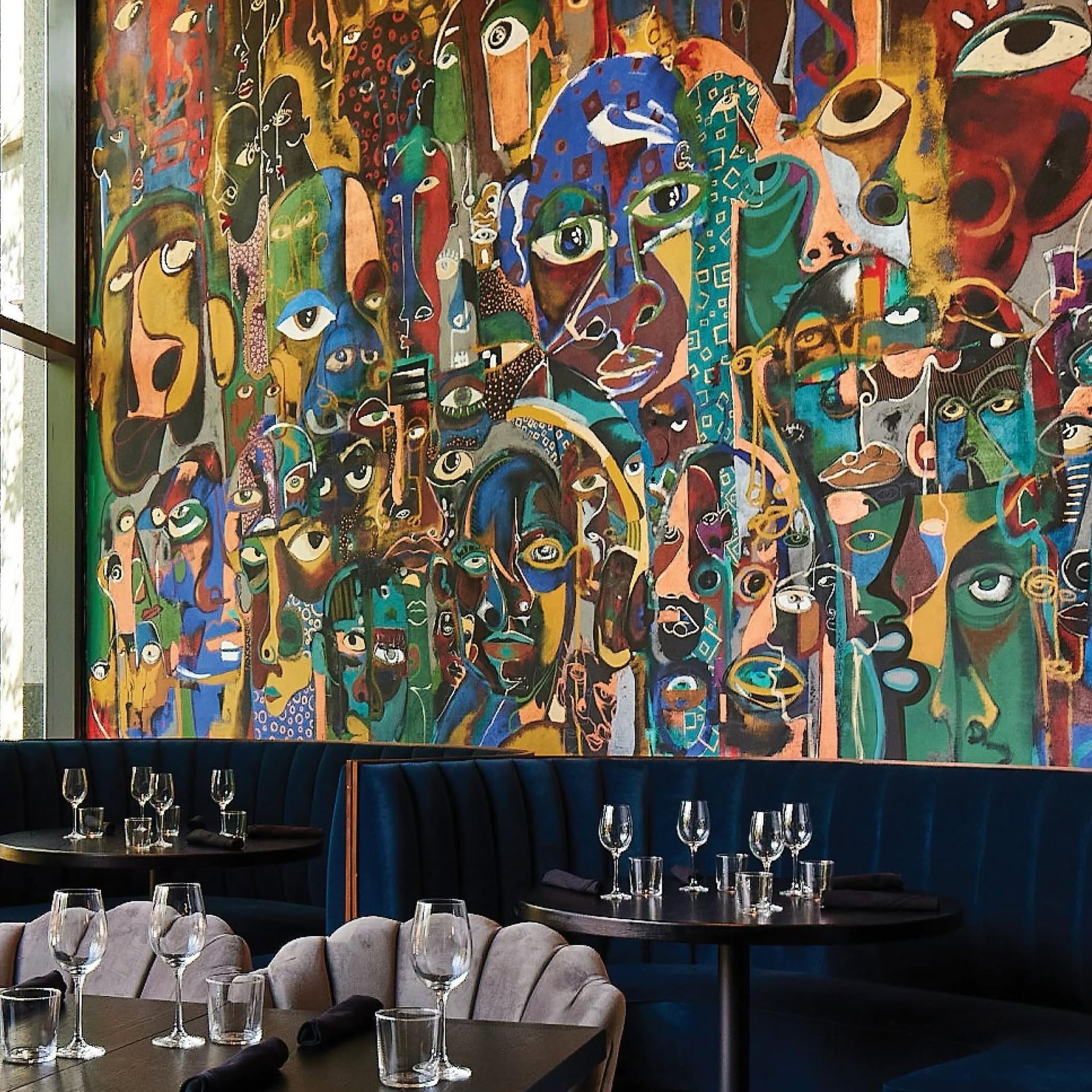 Colorful abstract mural above a restaurant dining area with dark tables and chairs